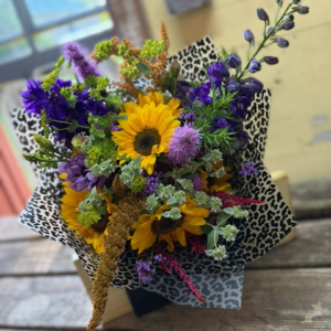 Wrapped bouquet of sunflowers, amaranth, delphinium, and more flowers.