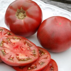 Three dark red, slightly mottled beefsteak-type tomatoes. One is sliced in four pieces